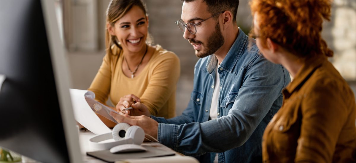 Group of young business colleagues analyzing reports in the offi Team of young business people going through paperwork while working together in the office. Focus is on businessman.
