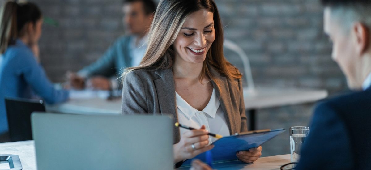 Happy financial advisor having a meeting with her client in the office. Young happy businesswoman reading reports while going through paperwork and working with a colleague in the office.